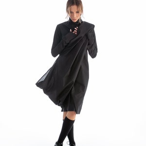 May include: A woman wearing a black dress with a long, flowing skirt. The dress has a high neck and long sleeves. She is wearing black socks and black shoes.