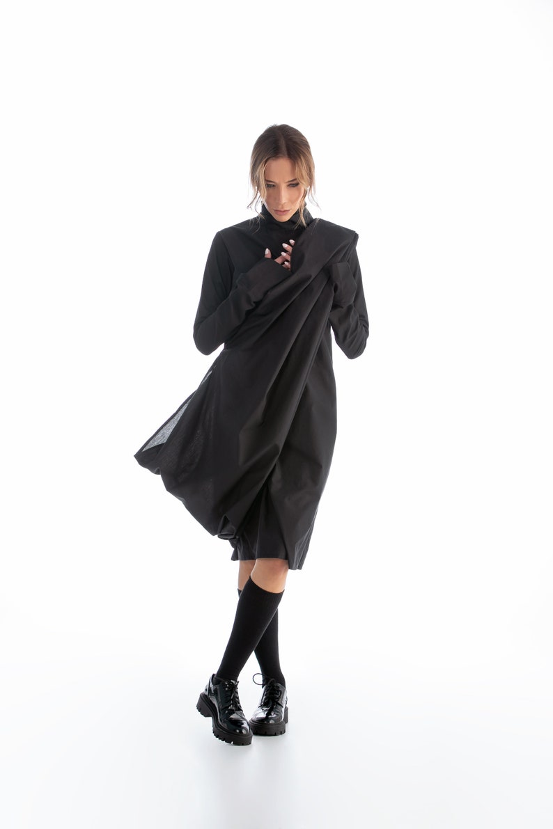 May include: A woman wearing a black dress with a long, flowing skirt. The dress has a high neck and long sleeves. She is wearing black socks and black shoes.