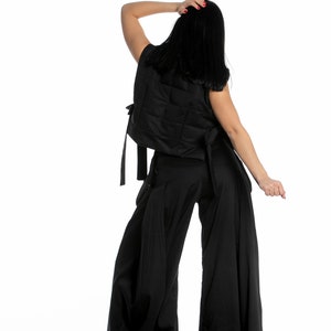 May include: A black sleeveless vest with a quilted design and a matching pair of wide-leg trousers. The vest has a tie at the back and the trousers have a wide waistband.