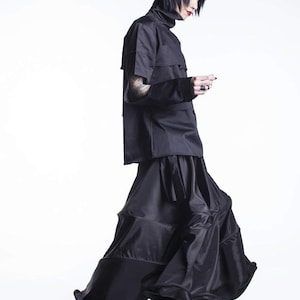 May include: A person wearing a black mock neck shirt with a layered skirt. The skirt has a ruffled hem and is made of a shiny fabric.