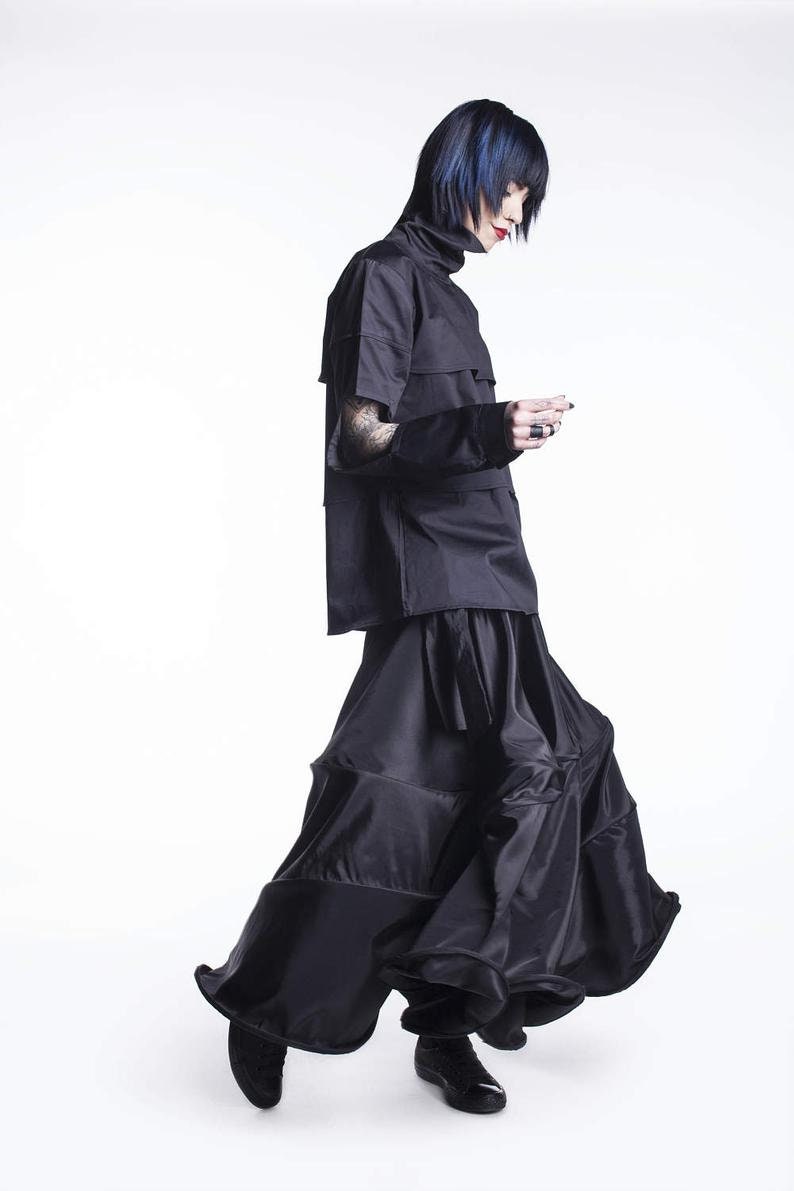May include: A person wearing a black mock neck shirt with a layered skirt. The skirt has a ruffled hem and is made of a shiny fabric.