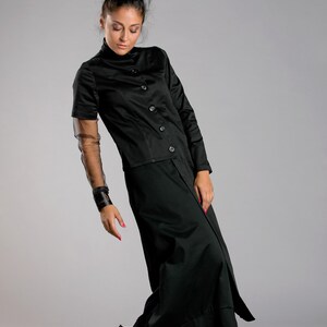 May include: A black ensemble featuring a button-down top with short sleeves and a long skirt. The outfit includes a sheer sleeve detail and a wide cuff bracelet. The model is wearing black shoes with colorful accents.