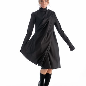 May include: A black long-sleeved dress with a draped design and a high neckline. The dress is worn with black knee-high socks and black patent leather shoes.
