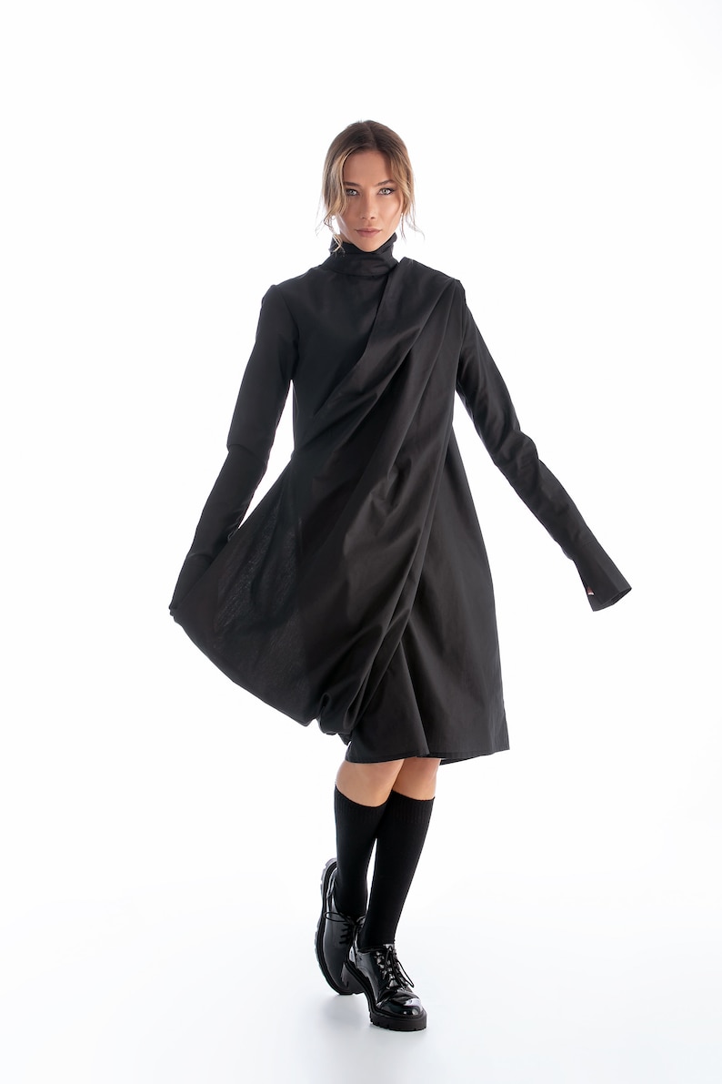 May include: A black long-sleeved dress with a draped design and a high neckline. The dress is worn with black knee-high socks and black patent leather shoes.