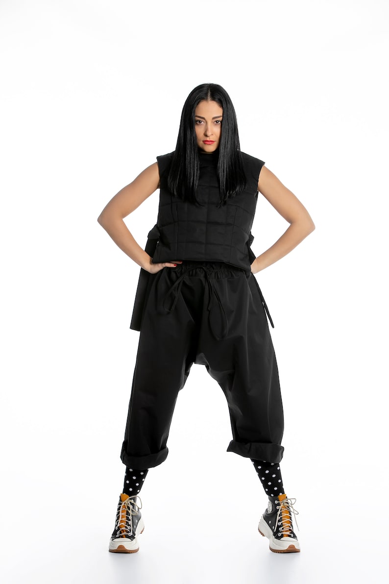 May include: A woman wearing a black quilted vest, black pants with a drawstring waist, black and white polka dot socks, and black and white sneakers with orange accents.
