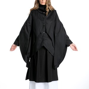 May include: A black long-sleeved shirt with a high collar and a layered design. The shirt has a button-up front and is worn with a black skirt and white underskirt.