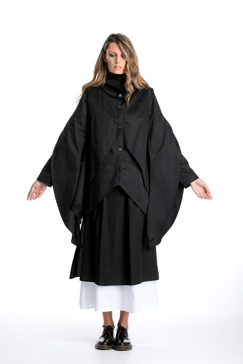 May include: A black long-sleeved shirt with a high collar and a layered design. The shirt has a button-up front and is worn with a black skirt and white underskirt.