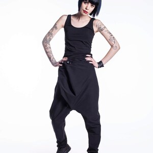 May include: A woman wearing a black tank top and black pants with a unique design. She has short, dark blue hair and tattoos on her arms.