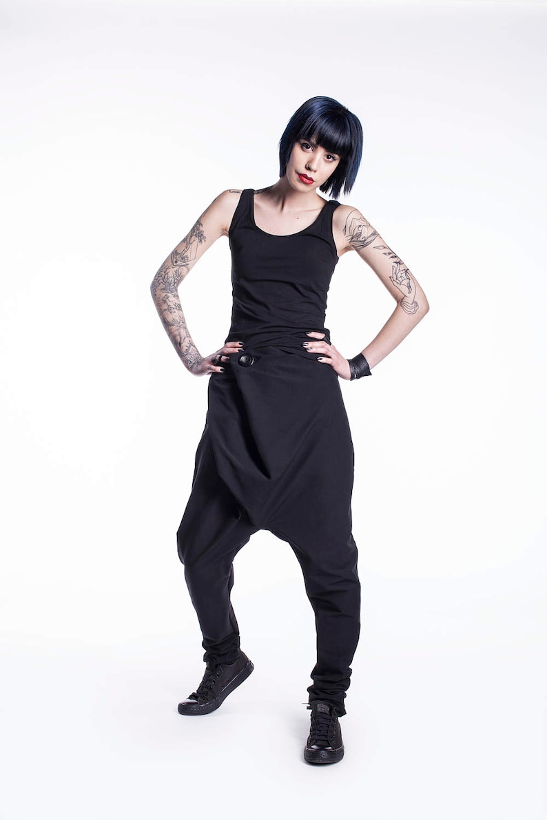 May include: A woman wearing a black tank top and black pants with a unique design. She has short, dark blue hair and tattoos on her arms.