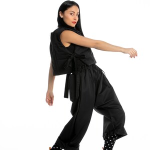 May include: A woman wearing a black puffer vest, black pants, and black and white polka dot socks. She is wearing black and white high-top sneakers with a brown sole.