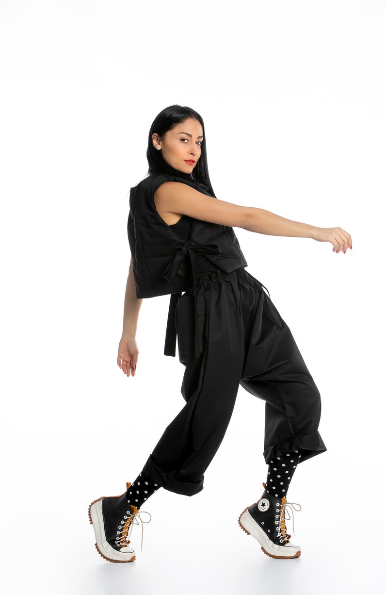 May include: A woman wearing a black puffer vest, black pants, and black and white polka dot socks. She is wearing black and white high-top sneakers with a brown sole.