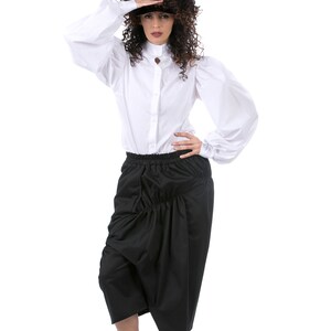 May include: A woman wearing a white button-down shirt with puffed sleeves and a black gathered skirt. She is wearing white sneakers.