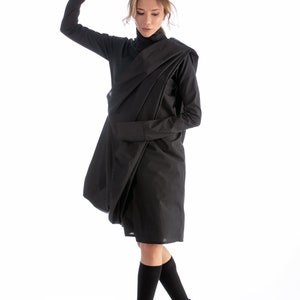 May include: A woman wearing a black, draped dress with long sleeves and black socks and shoes.