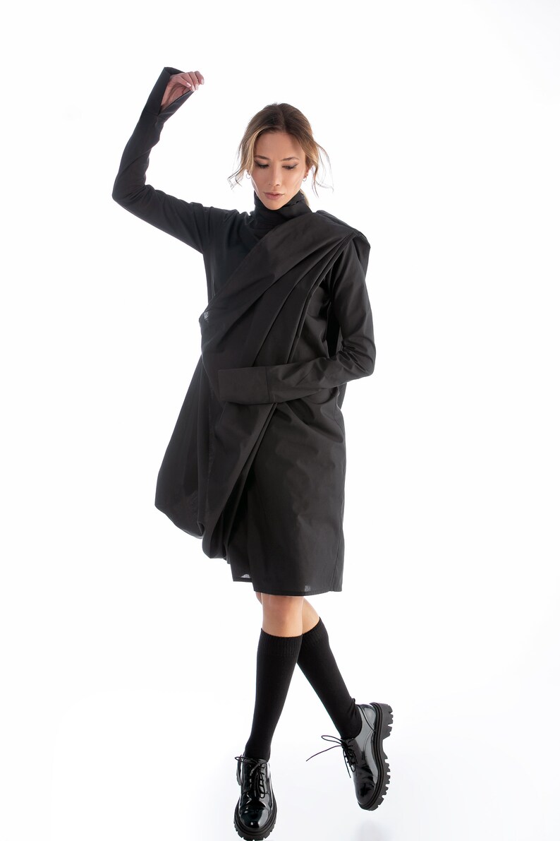 May include: A woman wearing a black, draped dress with long sleeves and black socks and shoes.