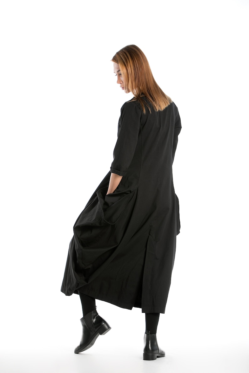 K&ouml;nnte beinhalten: Eine Frau in einem langen schwarzen Kleid mit gerafftem Rock und Taschen. Sie tr&auml;gt schwarze Stiefeletten und hat lange braune Haare.