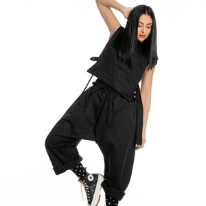 May include: A woman wearing a black quilted vest, black pants, and black and white polka dot socks. She is wearing black high-top sneakers with a white sole.