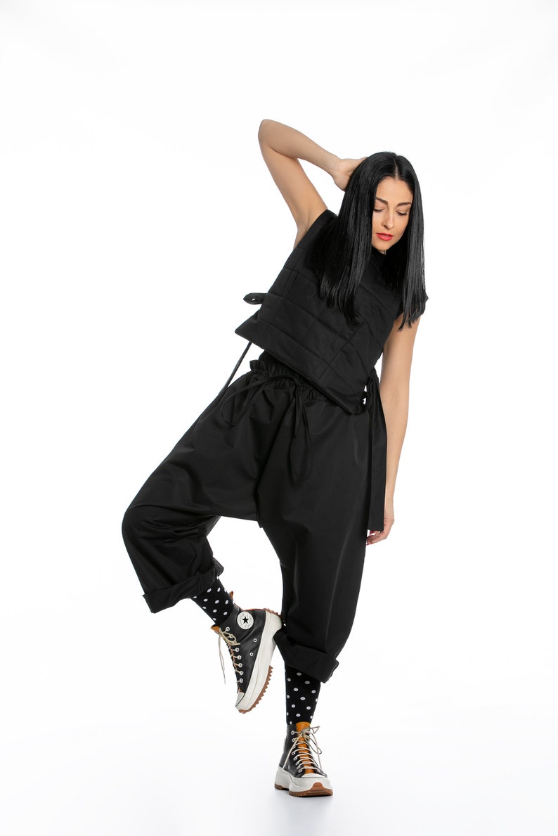 May include: A woman wearing a black quilted vest, black pants, and black and white polka dot socks. She is wearing black high-top sneakers with a white sole.