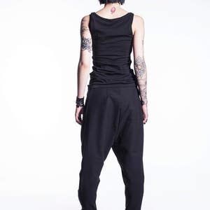 May include: A person wearing black pants and a black tank top. The person has short black hair and tattoos on their arms.