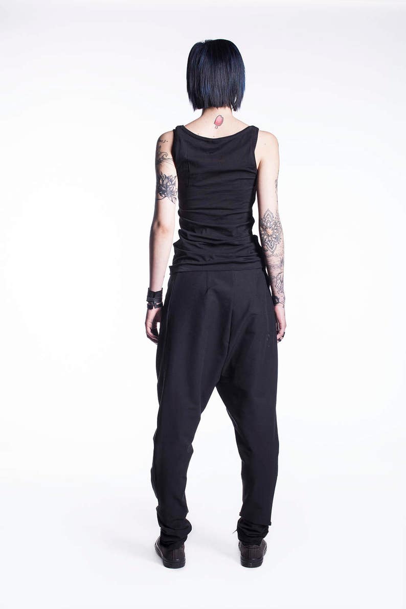 May include: A person wearing black pants and a black tank top. The person has short black hair and tattoos on their arms.
