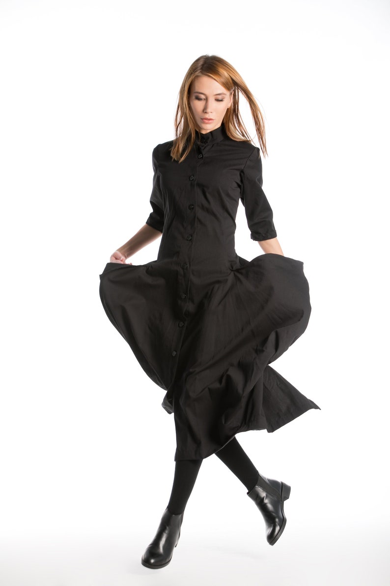K&ouml;nnte beinhalten: Eine Frau tr&auml;gt ein schwarzes Hemdblusenkleid mit langem Rock. Das Kleid hat einen Kragen und lange &Auml;rmel. Sie tr&auml;gt schwarze Strumpfhosen und schwarze Stiefeletten.