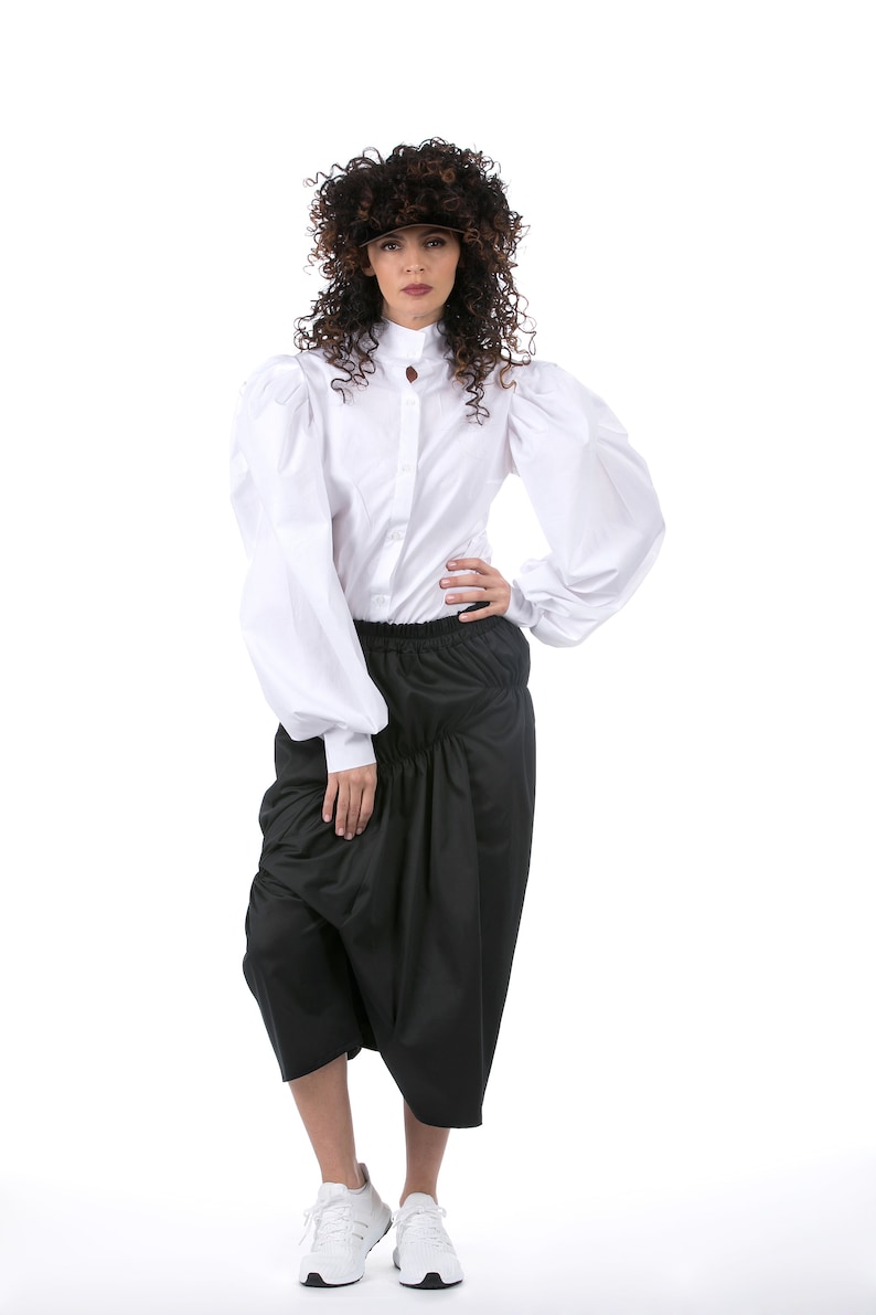 May include: A white button-up shirt with large, puffy sleeves and a black skirt with a gathered waist. The model is wearing white sneakers and a brown visor.