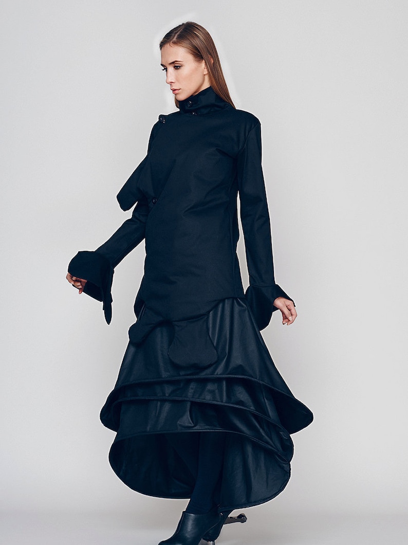 May include: A black long-sleeved shirt with a high collar and a layered skirt. The shirt has a unique design with a folded over collar and a long, flowing skirt.
