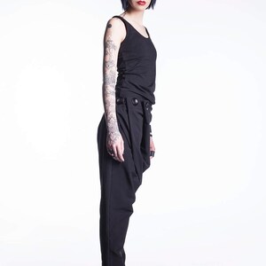 May include: A woman with short blue hair is wearing a black tank top and black pants with a unique design. She is wearing black sneakers and has tattoos on her arms.