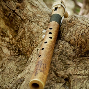 May include: A wooden flute with a brown finish and a carved design. The flute is resting on a tree branch.