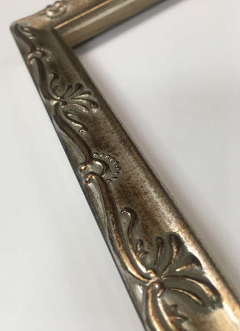 May include: A silver picture frame with ornate detailing. The frame has a distressed finish and a raised design.