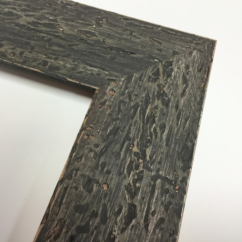 May include: Close-up of a corner of a dark grey wood picture frame with a distressed finish.