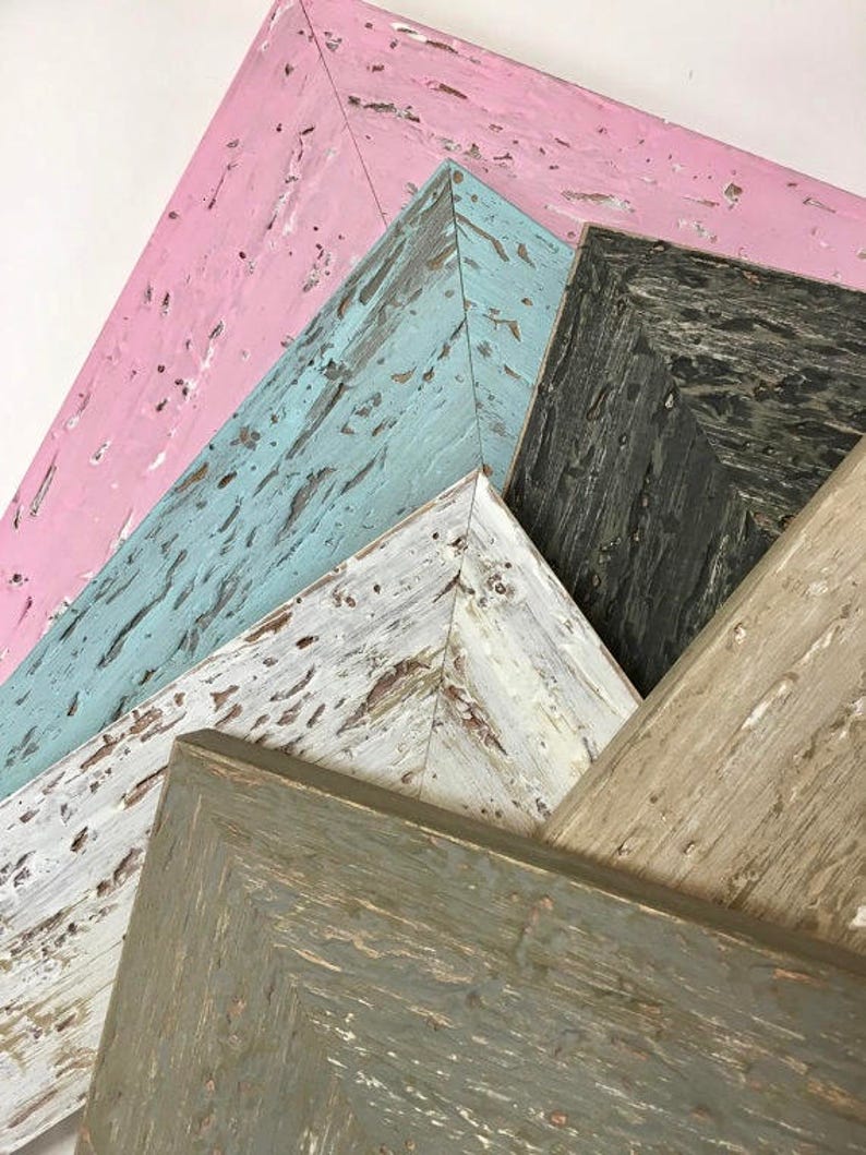 May include: Four wooden picture frames in various colours, including pink, blue, white, and grey. The frames are stacked on top of each other, with the pink frame on top and the grey frame on the bottom.