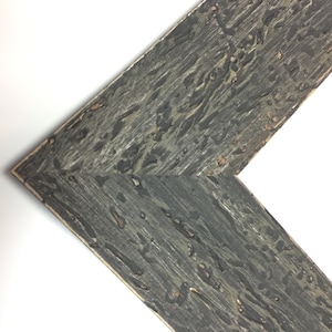 May include: Close-up of a corner of a dark grey wood picture frame with a distressed finish.
