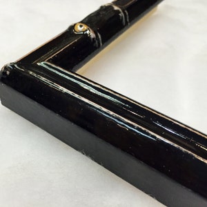 May include: Close-up of a black picture frame with a decorative bamboo design. The frame has a glossy finish and gold accents.