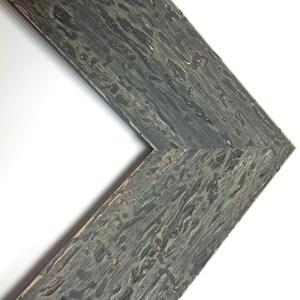 May include: Close-up of a corner of a dark grey wood picture frame with a distressed finish. The frame has a rustic look with knots and grain patterns.