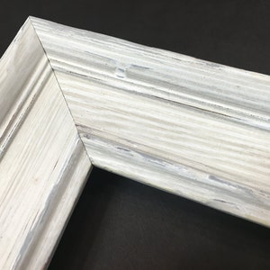 May include: Close-up of a white painted wooden picture frame with a distressed finish. The frame has a raised edge and a smooth surface.