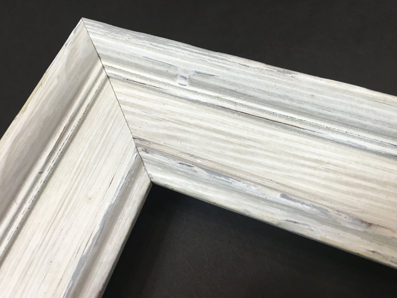 May include: Close-up of a white painted wooden picture frame with a distressed finish. The frame has a raised edge and a smooth surface.