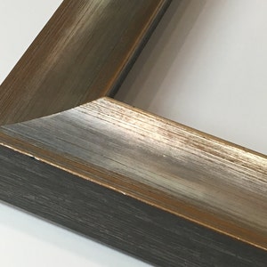 May include: Close-up of a corner of a picture frame with a distressed wood finish. The frame has a dark brown base with a silver and gold metallic overlay.
