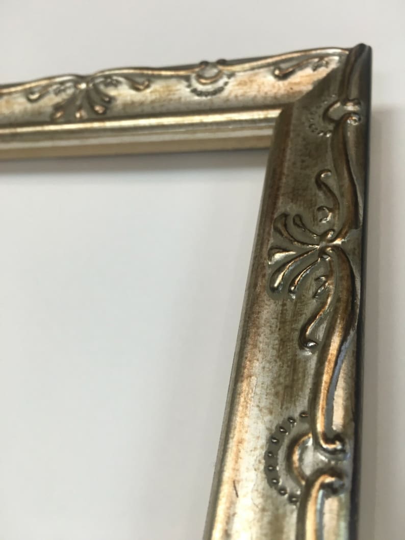 May include: A silver picture frame with ornate detailing around the edges. The frame has a slightly distressed look, giving it a vintage feel.