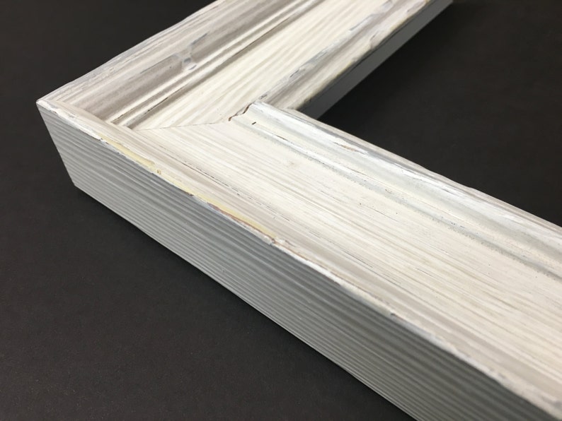 May include: Close-up of a white wood picture frame with a distressed finish. The frame has a raised edge and a simple design.