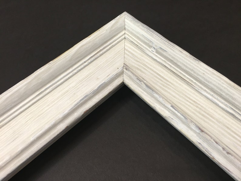 May include: Close-up of a white painted wooden picture frame with a distressed finish. The frame has a simple, classic design with a slightly raised edge.