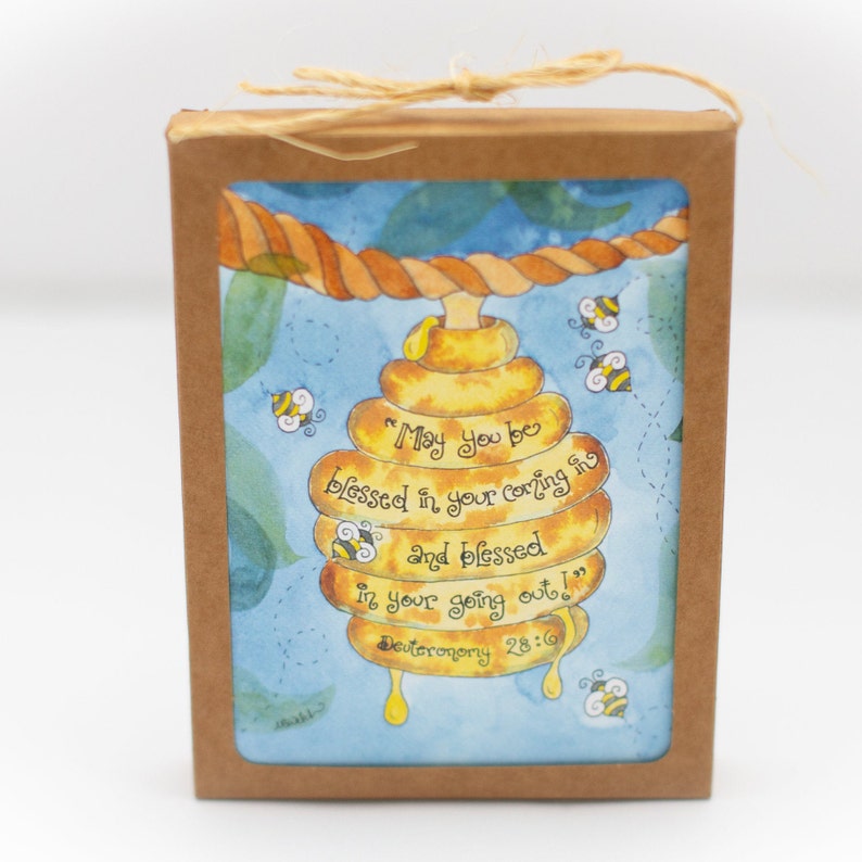 May include: A boxed gift with a watercolour illustration of a beehive. The text reads "May you be blessed in your coming in and blessed in your going out!" and Deuteronomy 28:6. The background is blue with bees.