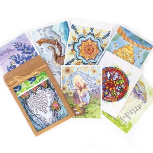 May include: A selection of watercolour art cards with diverse designs, such as floral patterns, celestial themes, and inspirational quotes. The cards are packaged in a brown paper sleeve tied with twine, displaying a preview of the artwork.