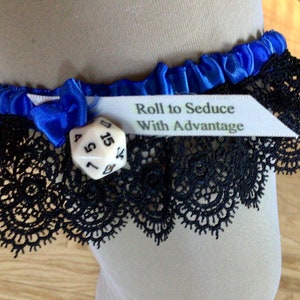 May include: A blue satin garter with black lace trim and a small blue bow. A white tag reads "Roll to Seduce With Advantage." A white, multi-sided die is attached.