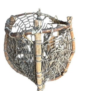 May include: A woven basket made of natural materials, with a circular base and a woven top. The basket is made of brown twigs and has a light gray woven pattern.