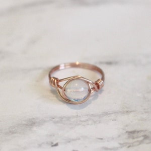 Puede incluir: Un anillo de alambre envuelto en oro rosa con una piedra preciosa transparente iridiscente.