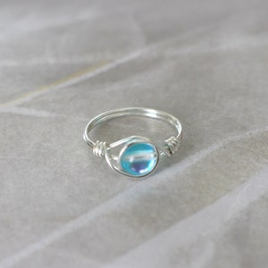 Puede incluir: Un anillo de plata con una piedra azul iridiscente engastada en el centro.