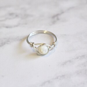 May include: A silver wire wrapped ring with a white pearl-like stone in the centre.