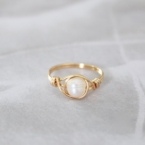 May include: A gold ring with a white pearl set in the centre. The ring is made of wire that is wrapped around the pearl.