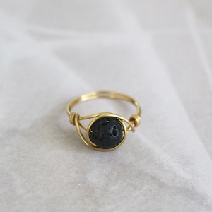 Può includere: Un anello di filo d'oro con una pietra di lava nera.