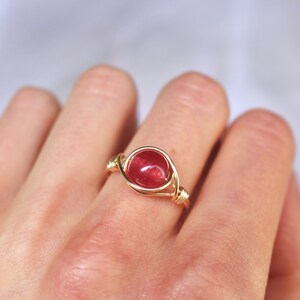 May include: A gold wire wrapped ring with a round, red gemstone.